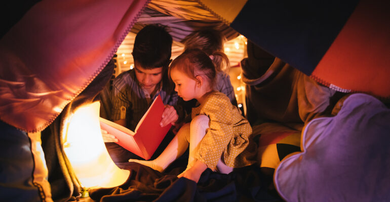 Children reading a story in blanket fort at night