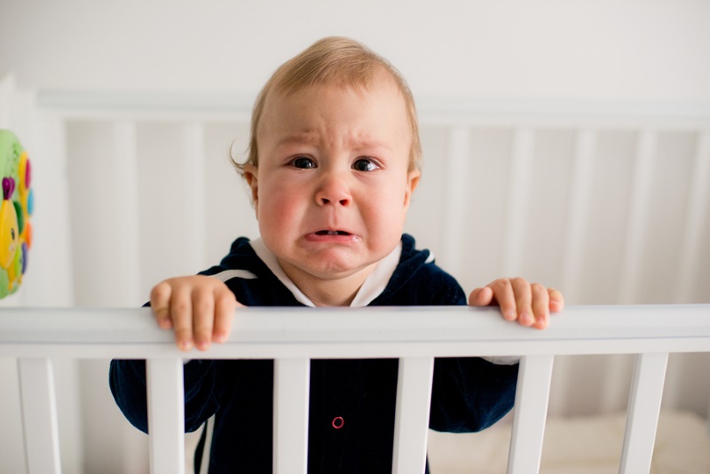 The baby cries and calls mom from a bed