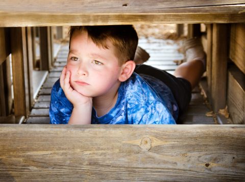 Unhappy child hiding and sulking while playing on playground