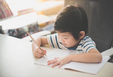 child  using a pencil to write on notebook