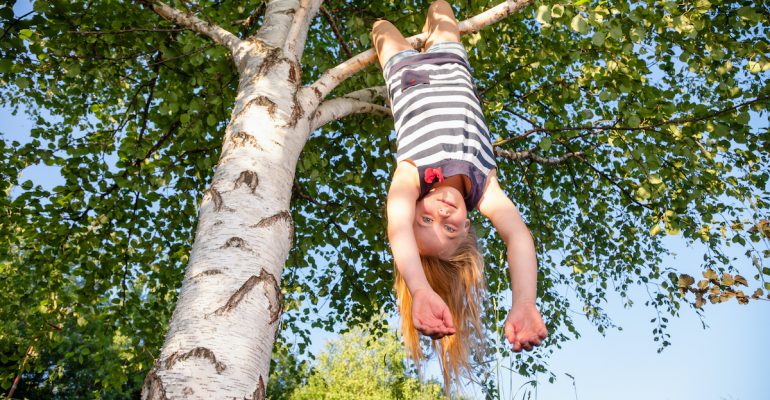 Happy girl hanging from a tree in a summer park